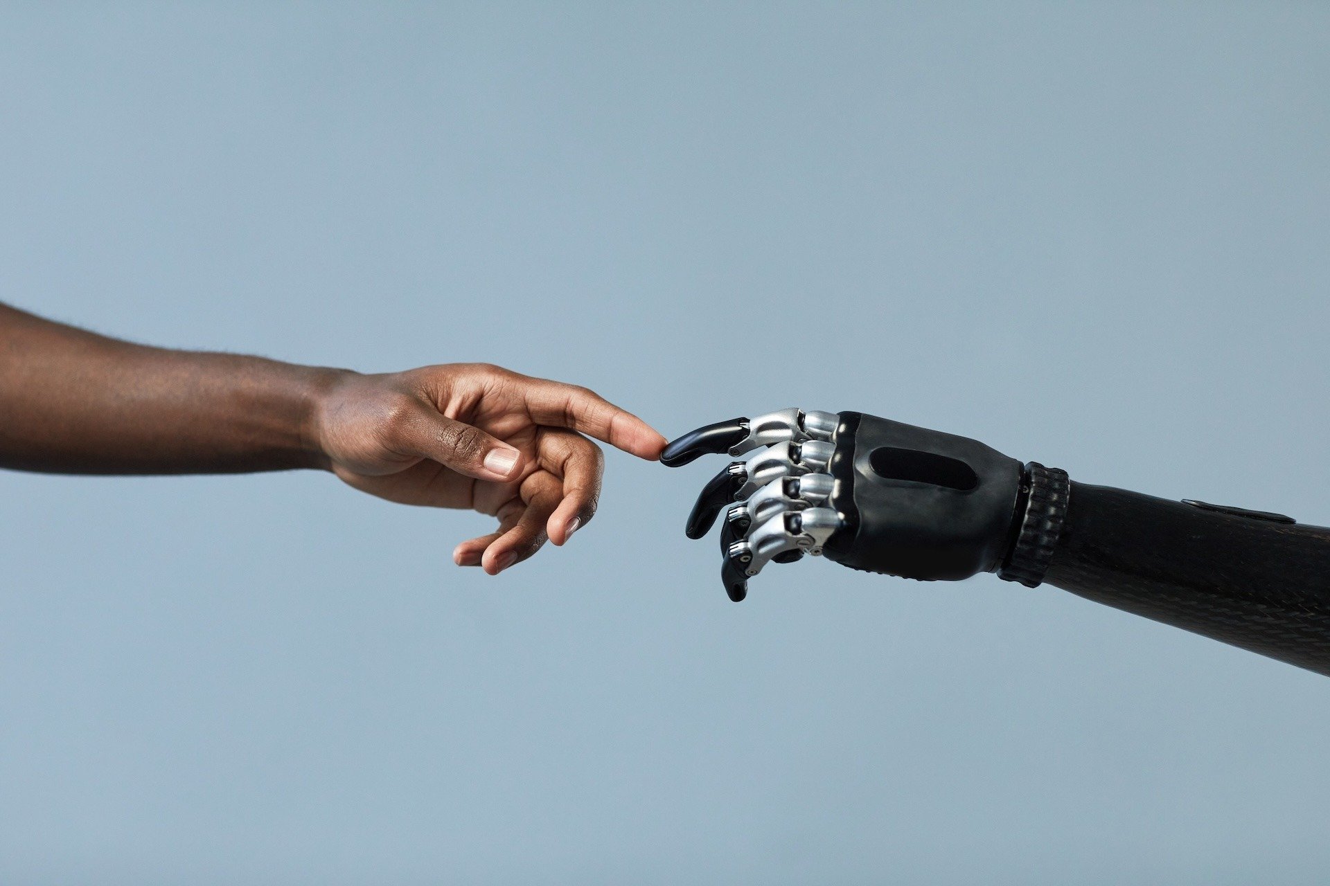 Image of a human hand touching fingertips of a robotic arm, conveying the collaboration of humans and AI.